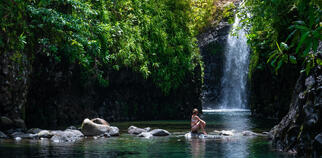 Image of woman sitting on rocks in front of waterfall