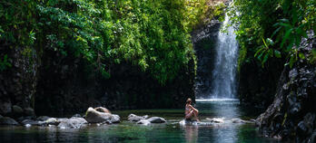 Image of woman sitting on rocks in front of waterfall
