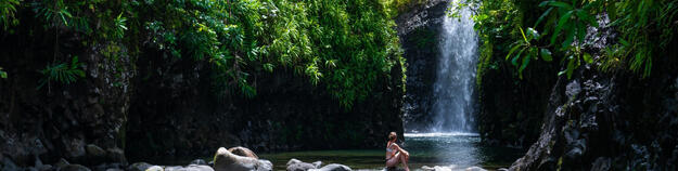 Image of woman sitting on rocks in front of waterfall