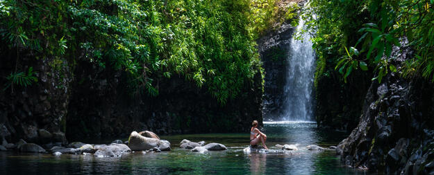 Image of woman sitting on rocks in front of waterfall