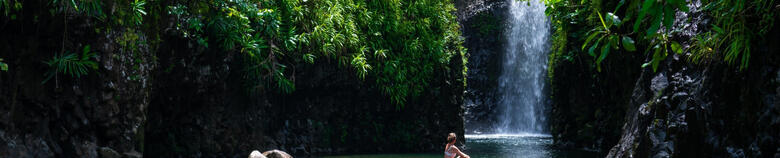 Image of woman sitting on rocks in front of waterfall