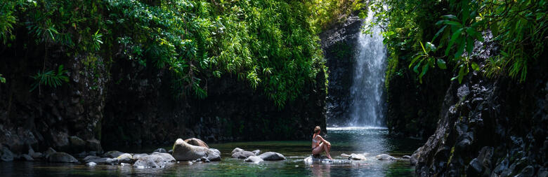 Image of woman sitting on rocks in front of waterfall