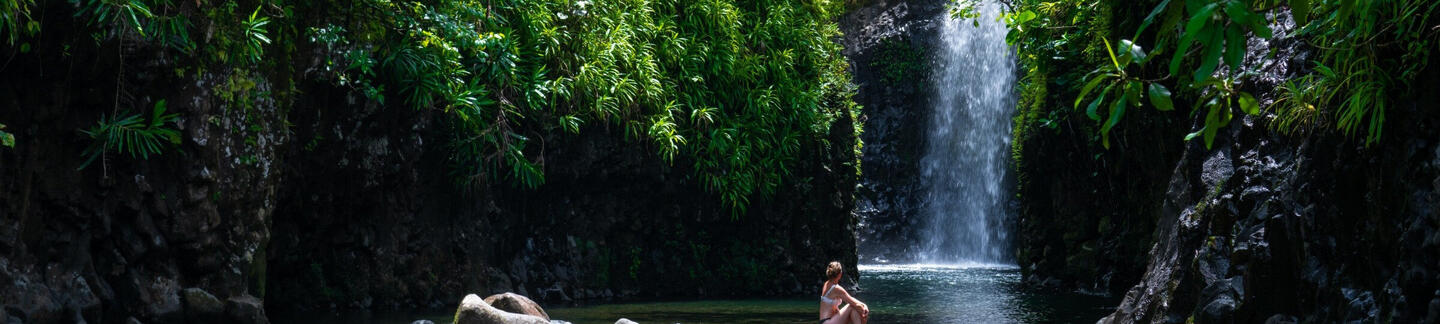 Image of woman sitting on rocks in front of waterfall