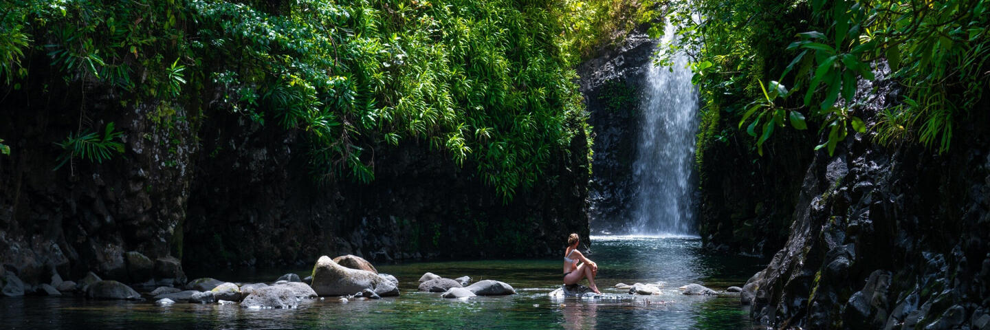 Image of woman sitting on rocks in front of waterfall