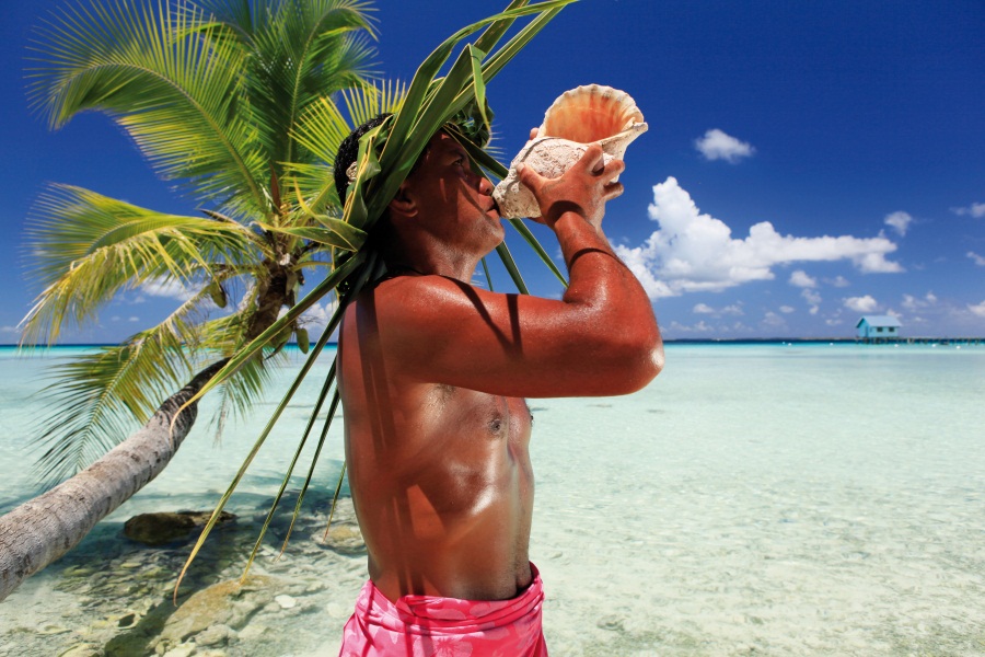 Tahitian man with woven hat blows the conch shell on the beach