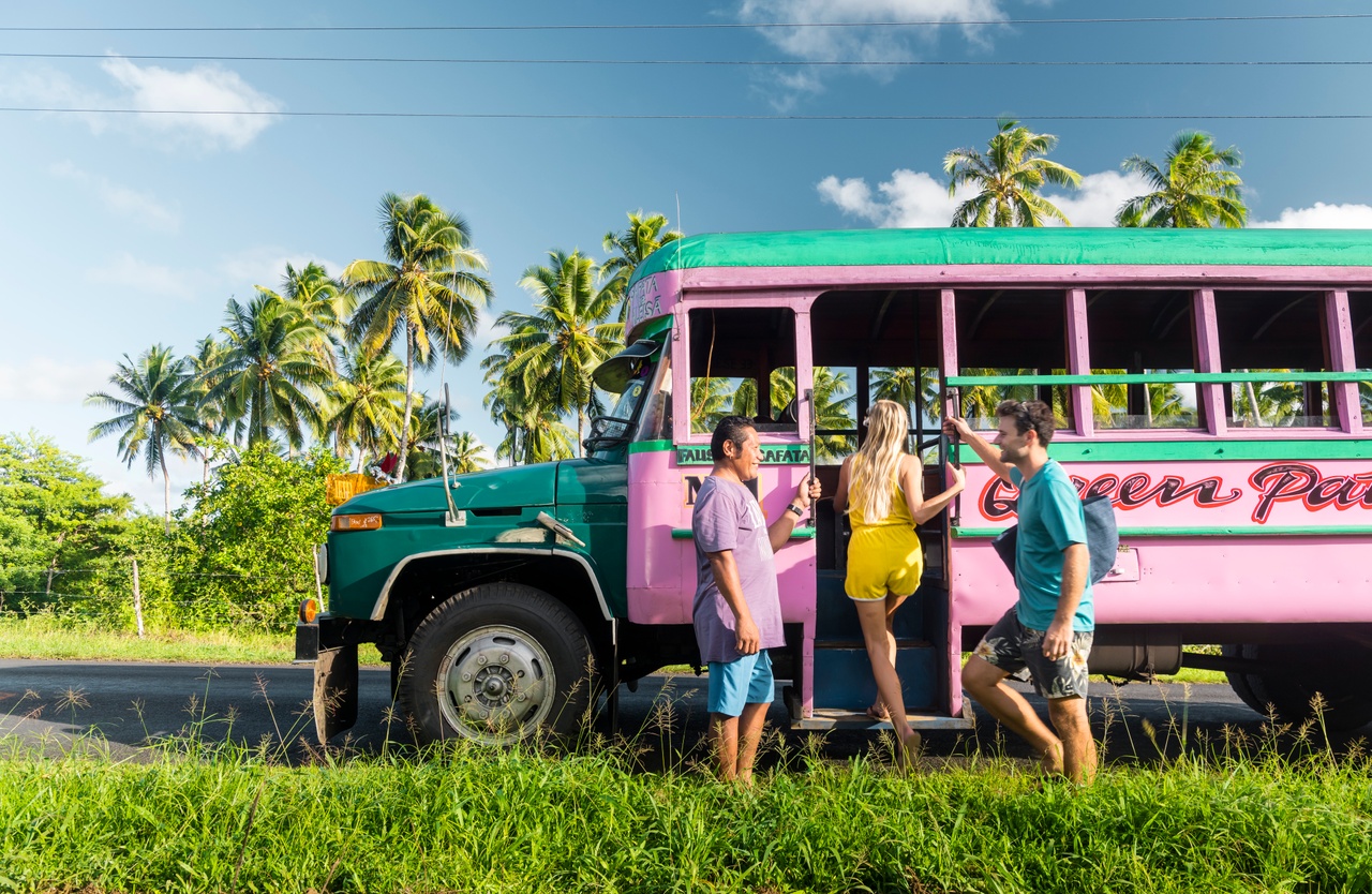 Couple boards a bright pink bus on the side of the road