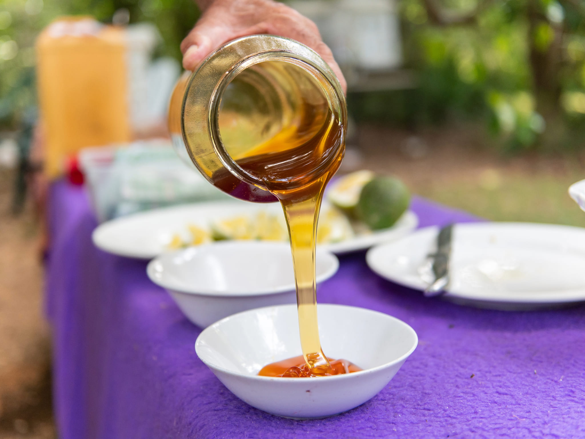 Honey is poured from a glass jar into a white bowl, on a table display