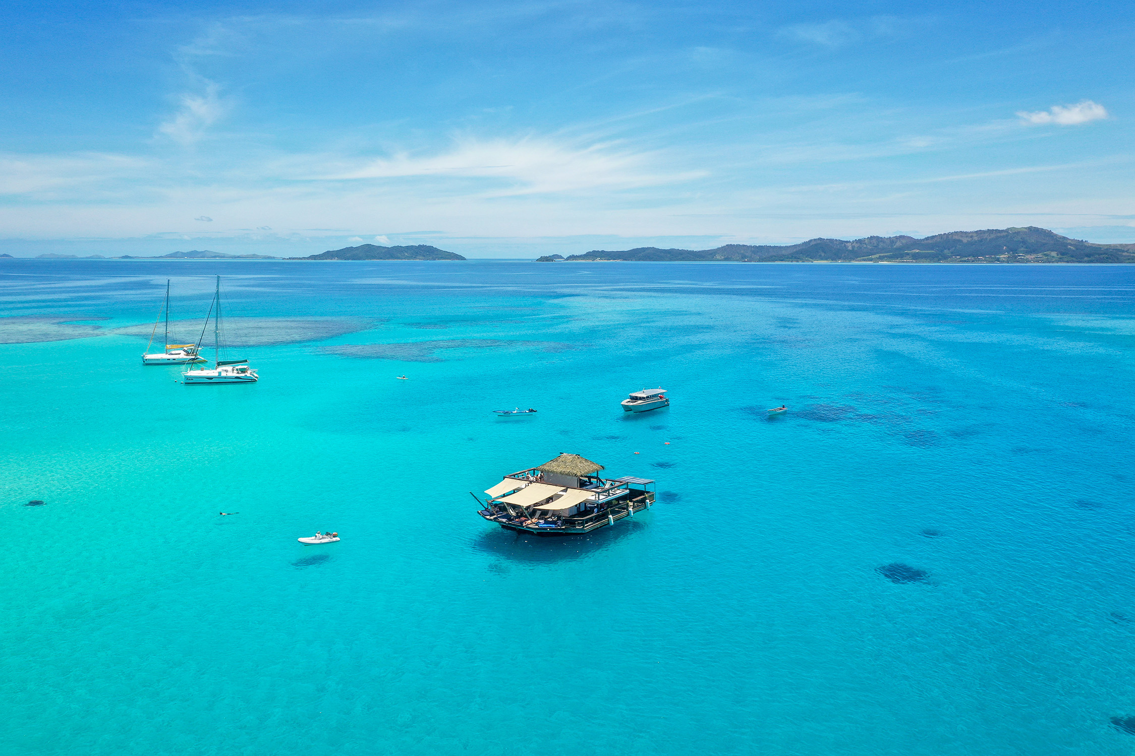 An aerial view of Cloud 9 floating on azure waters with a dottering of sail boats nearby.