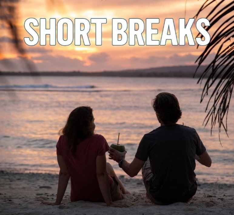 Couple sits on the beach at sunset drinking a coconut