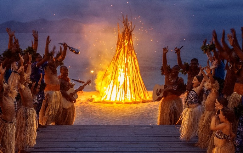 Group of local Fijians celebrating with Travellers by the fire with song and dance