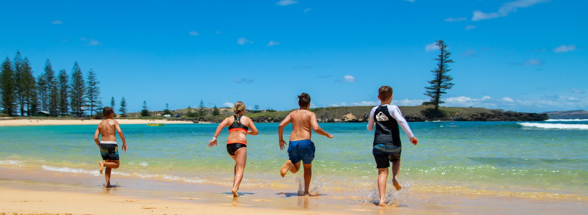 Family running into the ocean from beach on Norfolk Island