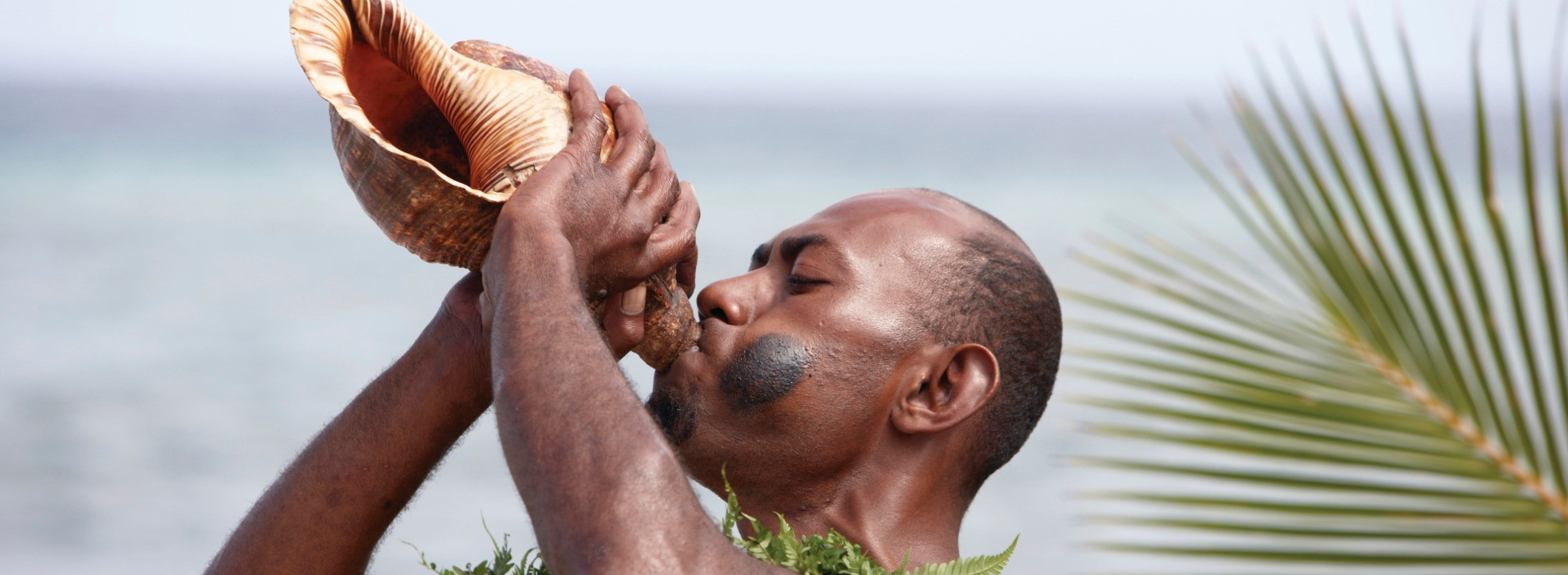 Image of a man in traditional dress blowing a Conch shell