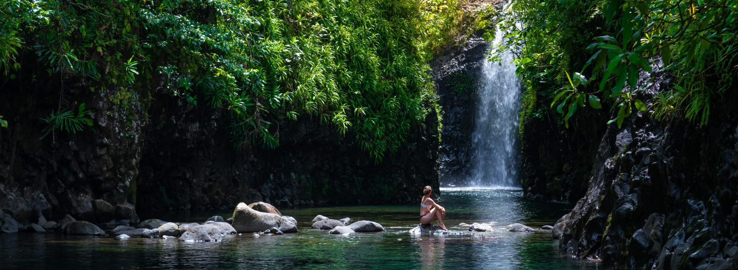 Image of woman sitting on rocks in front of waterfall